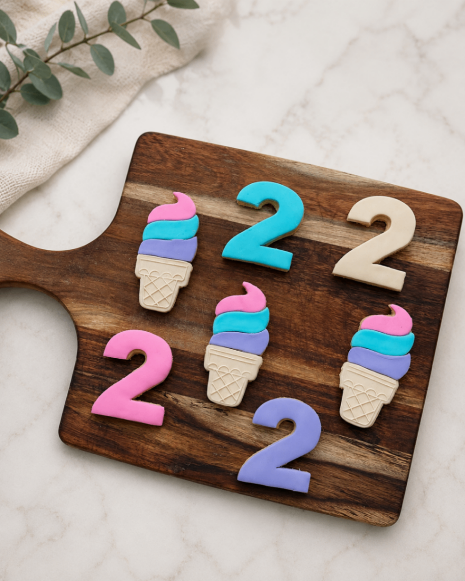 Number 2 and ice cream cone sugar cookies in pink, teal and purple on a wooden board