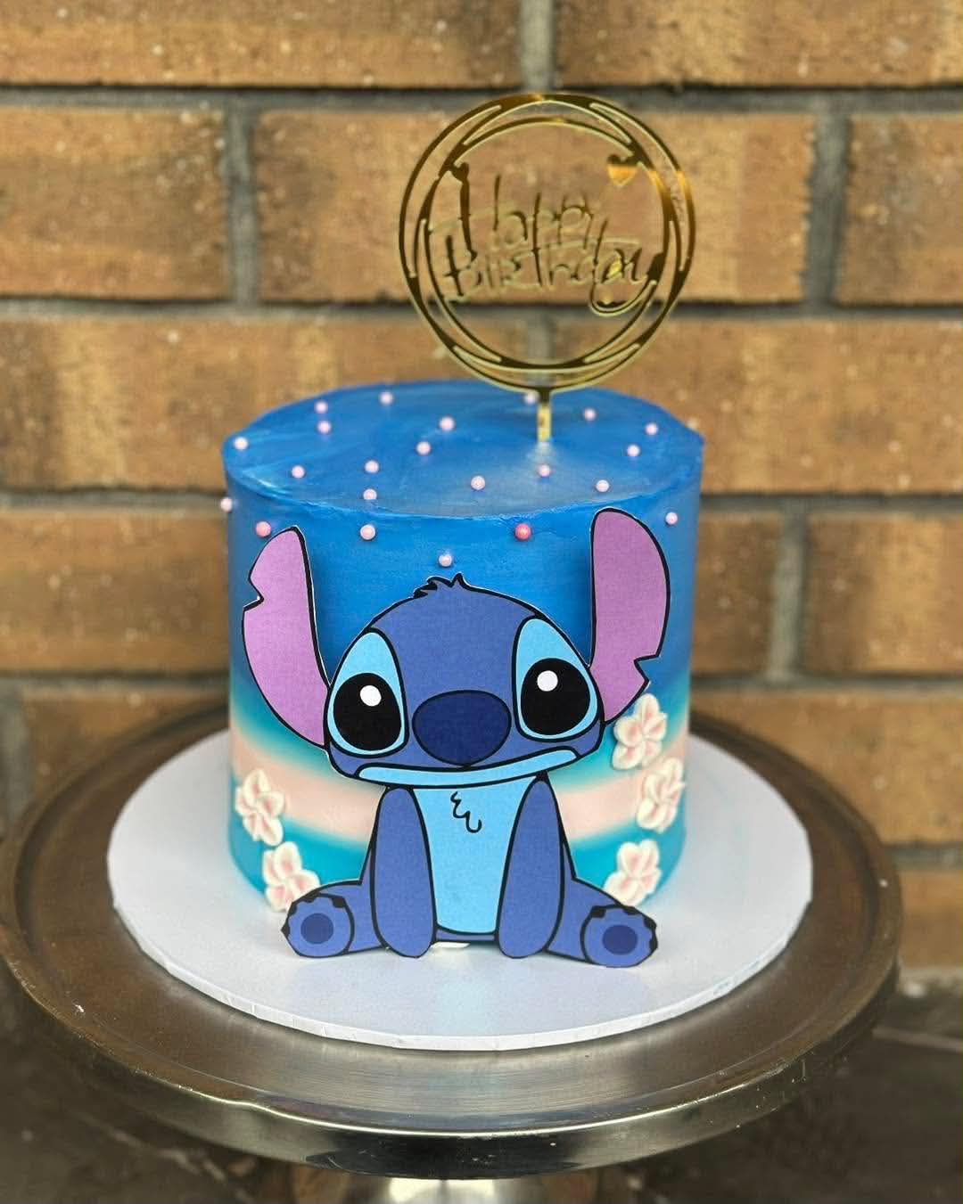 Blue ombre Stitch birthday cake with Lilo and Stitch edible print, white hibiscus flowers and gold Happy Birthday topper