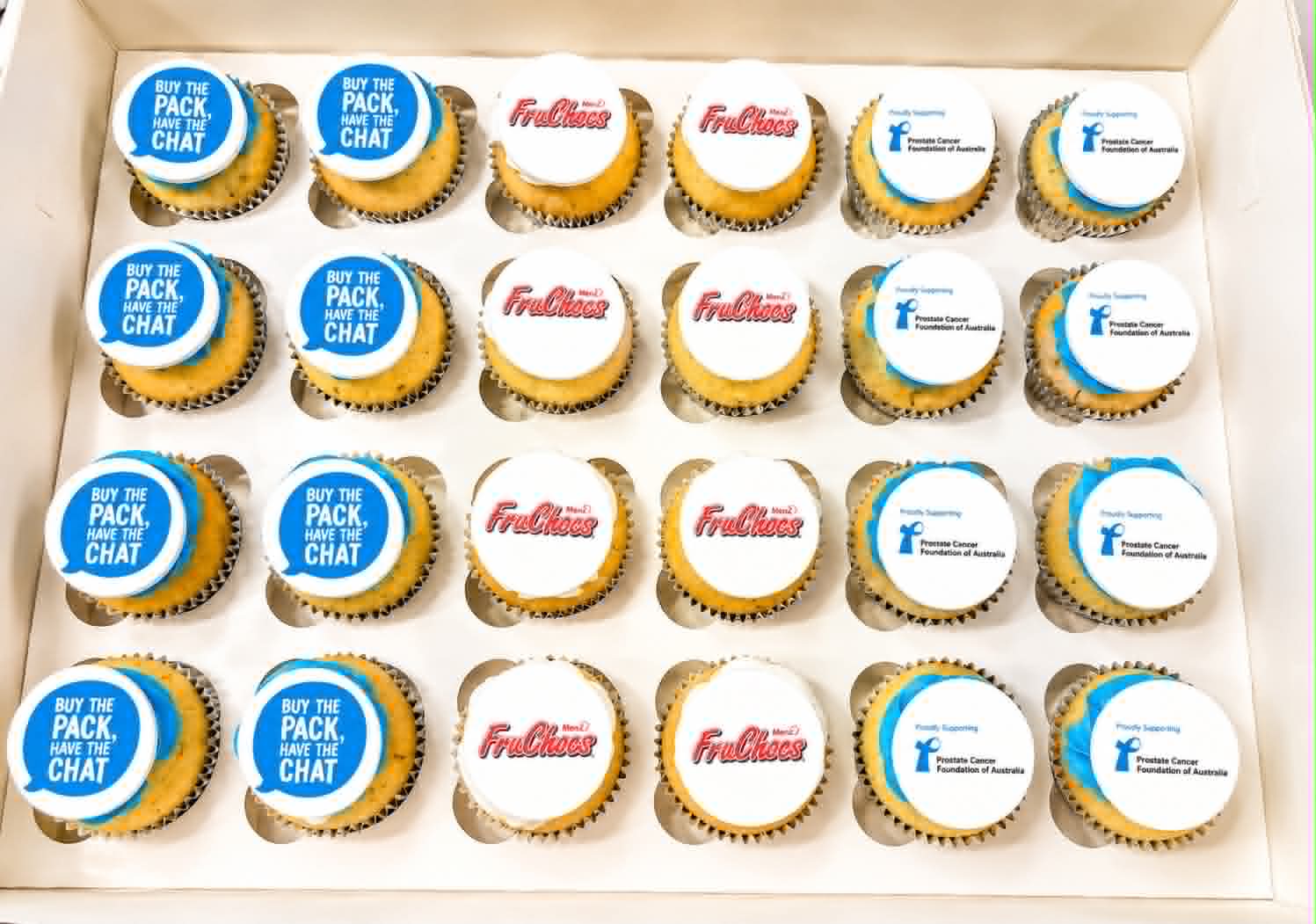 Large box of 24 vanilla cupcakes with white fondant toppers in three designs — blue Buy the Pack Have the Chat, FruChocs Menz red logo, and Prostate Cancer Foundation of Australia
