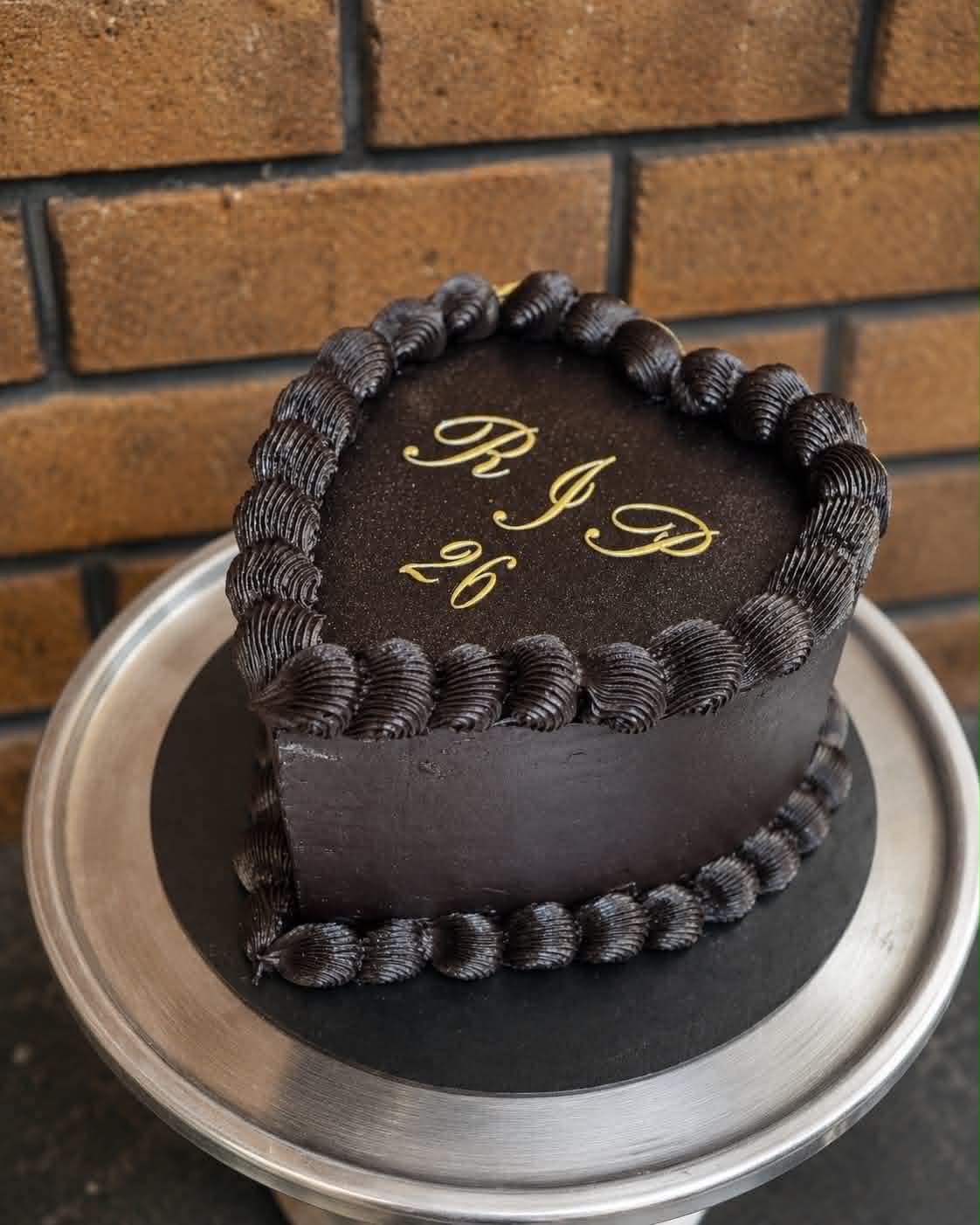 Dark chocolate heart cake with gold script reading RIP 26 and chocolate shell piping