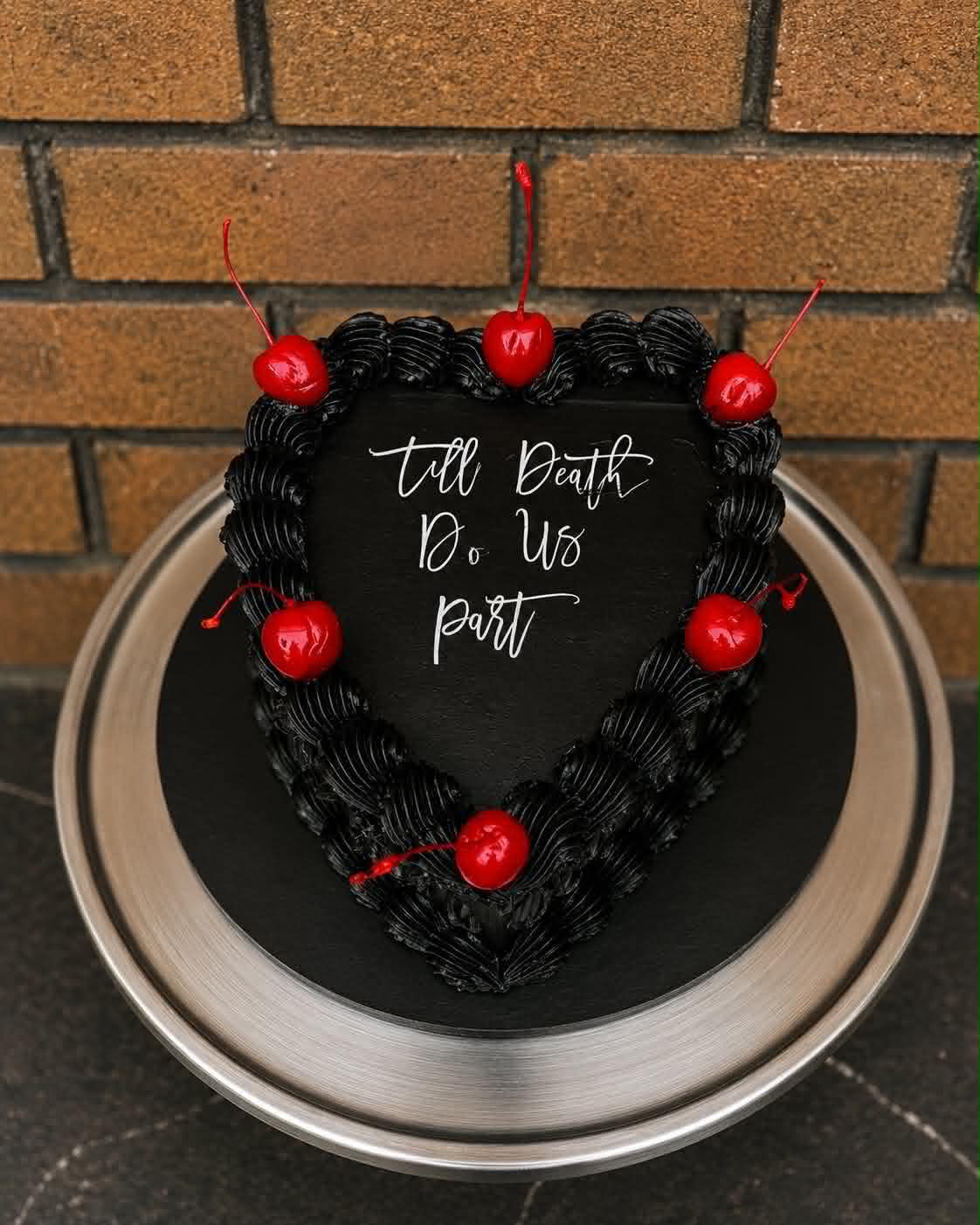 Black heart cake with white script reading Till Death Do Us Part and red cherries