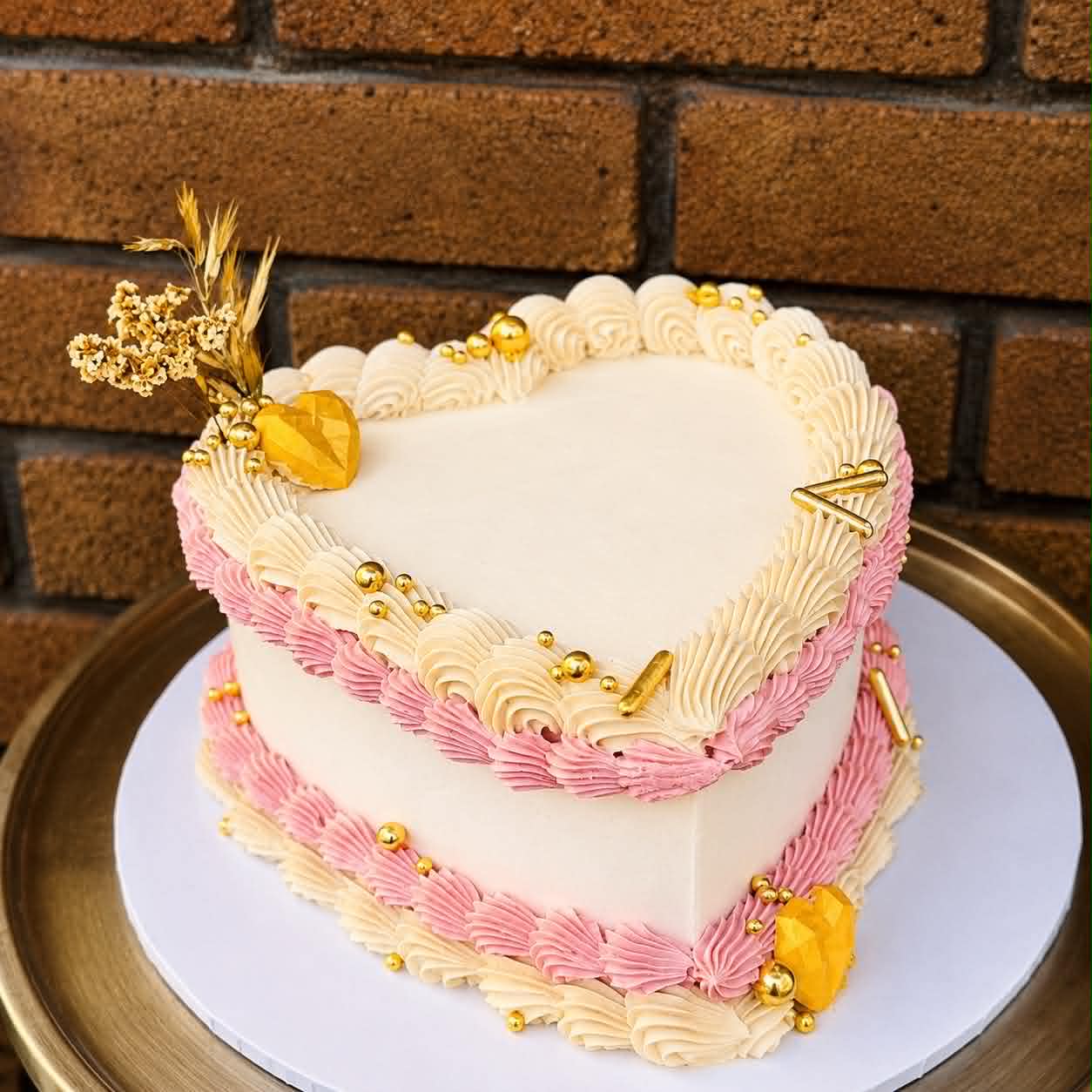 White and pink heart cake with shell buttercream piping, gold pearl balls, gold dried flowers and amber crystal decorations