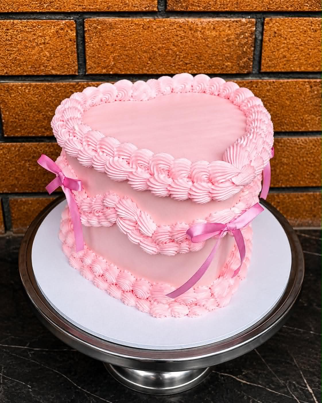 Two-tier all-pink heart cake with rosette and shell buttercream piping and pink satin ribbon bows