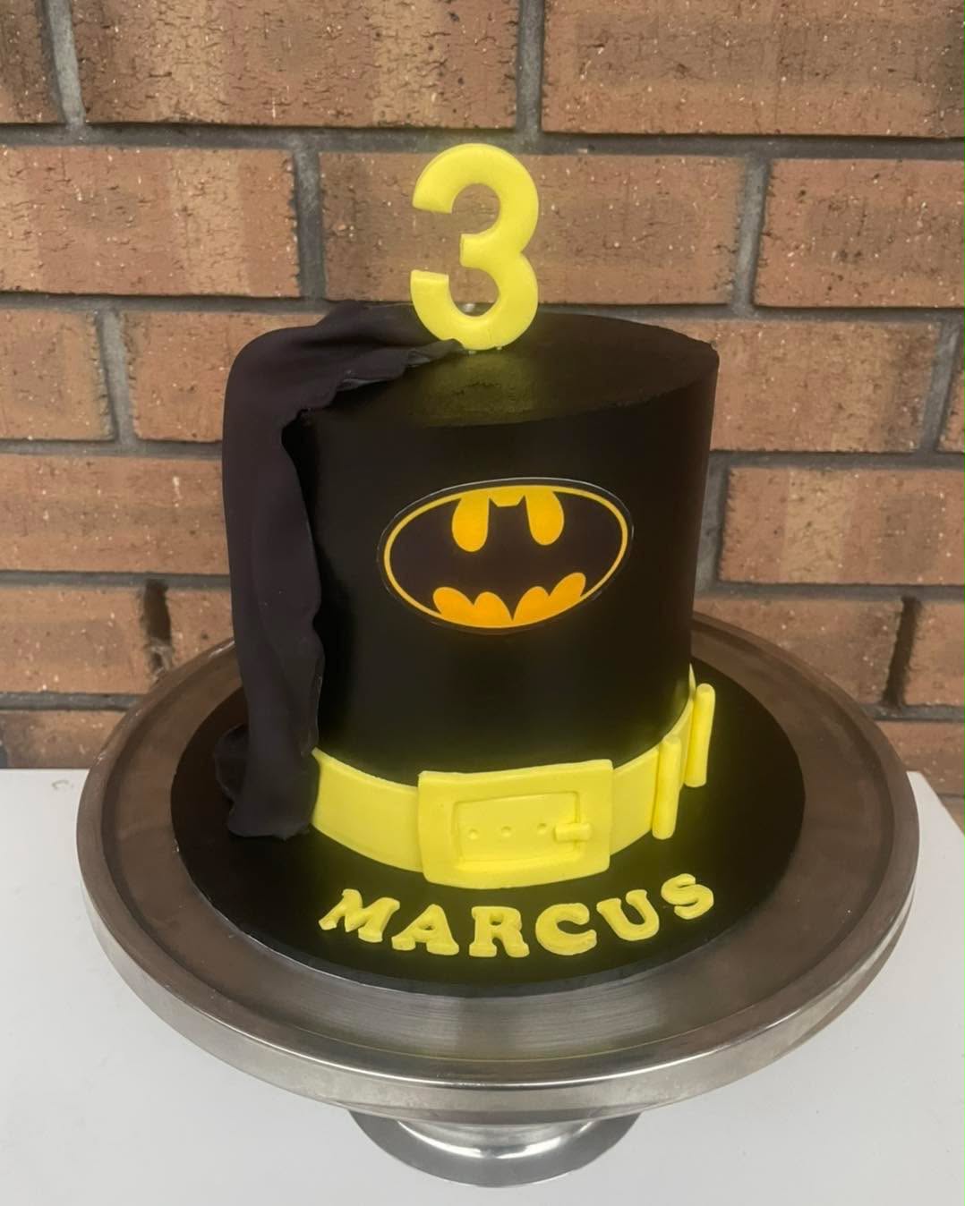 Black fondant Batman cake for Marcus's 3rd birthday with yellow Batman logo, fondant cape, yellow utility belt and yellow number 3 candle topper