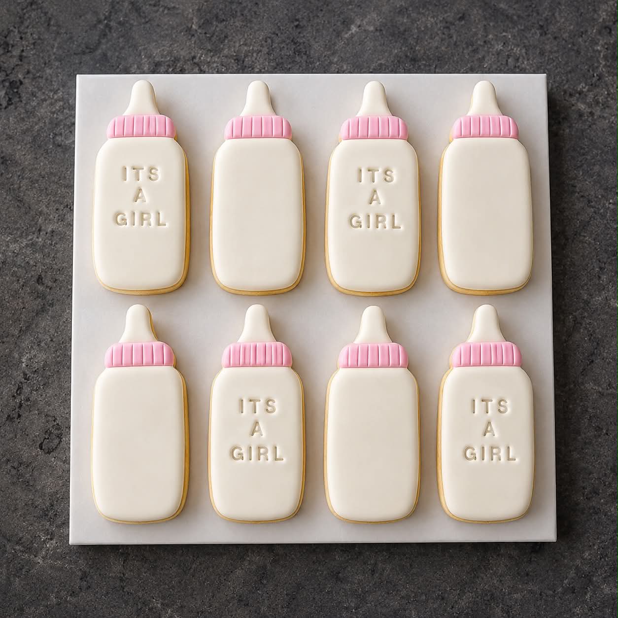 Eight white and pink It's A Girl baby bottle shaped sugar cookies on a white marble board
