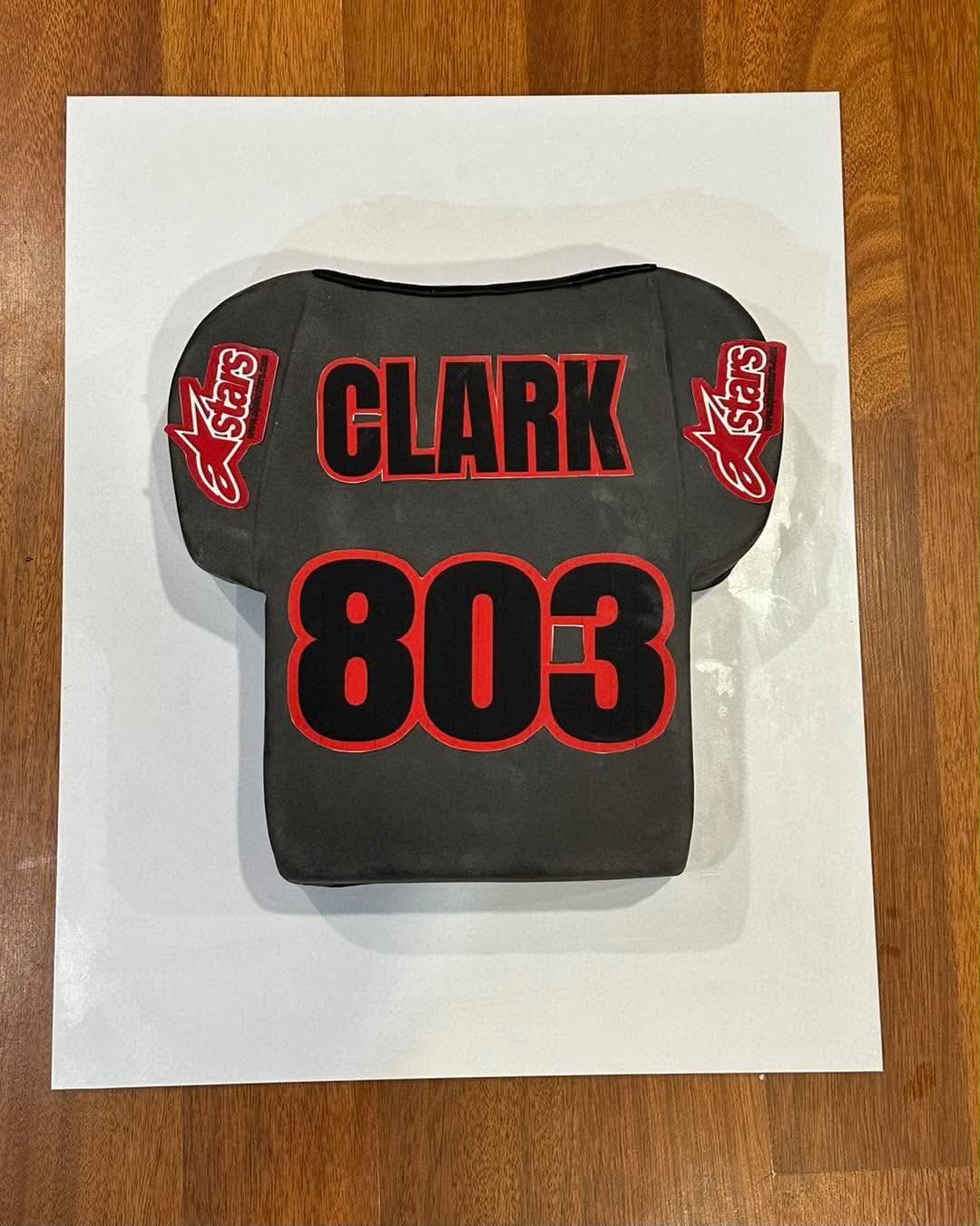 Black motocross jersey shaped birthday cake for Clark 803 with red Alpinestars logo patches and number 803