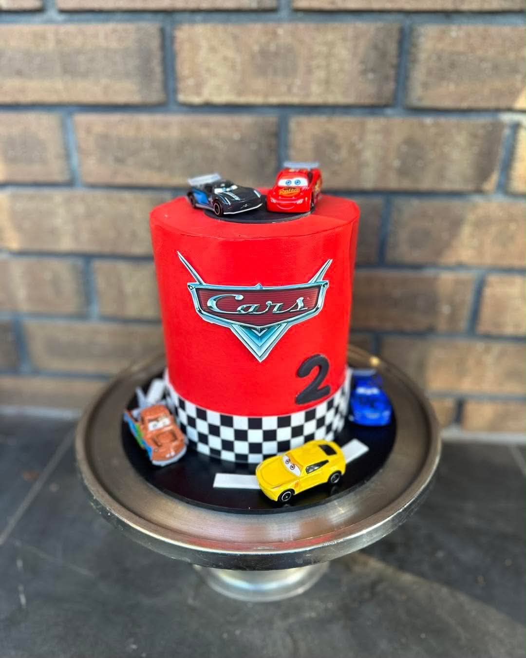 Red Disney Cars birthday cake for 2nd birthday with Cars logo, Lightning McQueen and Jackson Storm toppers and checkered border