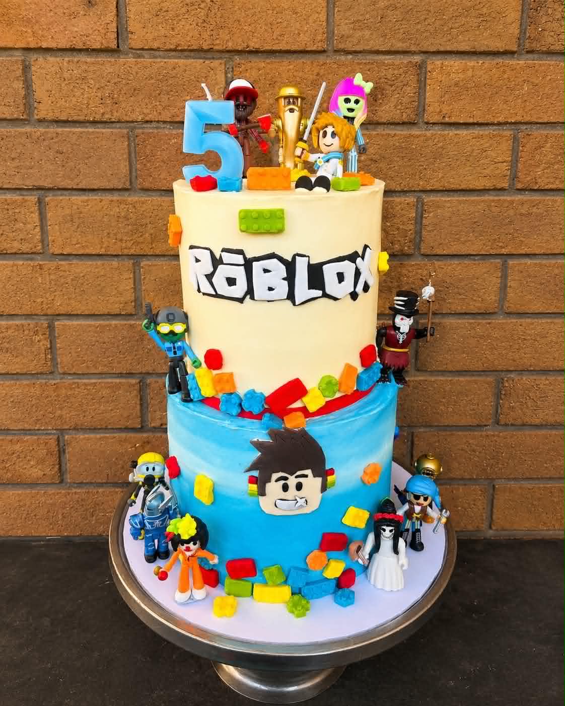 Two-tier Roblox birthday cake with blue and cream fondant, Roblox character figurines and colourful brick decorations
