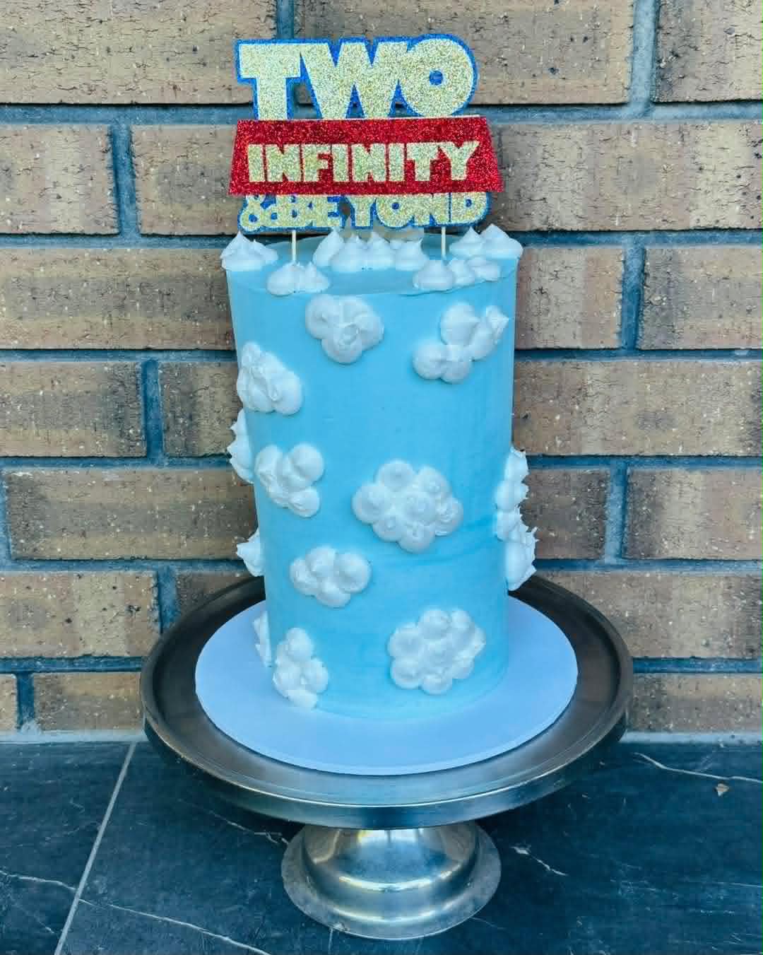 Tall blue sky birthday cake with white cloud buttercream and Two Infinity and Beyond glitter topper
