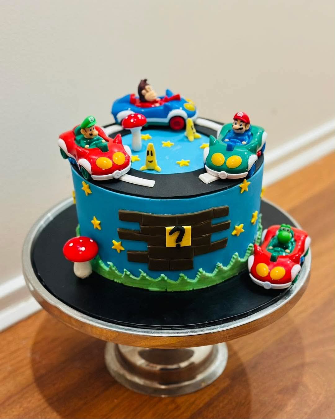 Blue Mario Kart birthday cake with Mario, Luigi, Donkey Kong and Yoshi kart figurines, question block and mushroom decorations