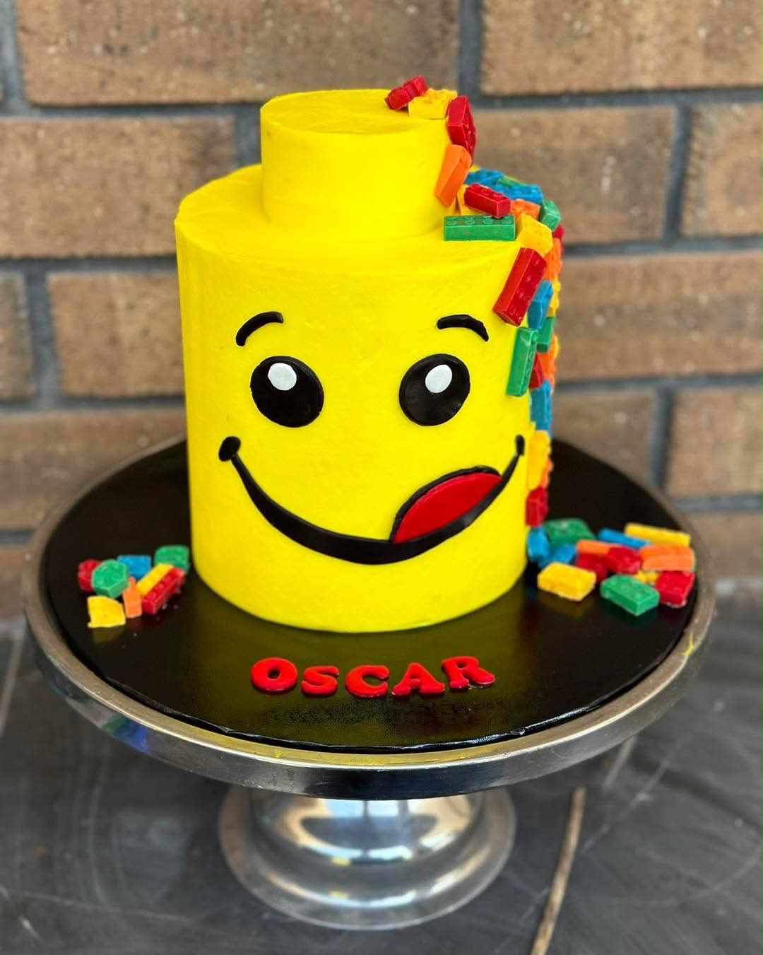 Yellow Lego head birthday cake for Oscar with smiley face, tongue and colourful Lego brick explosion on top