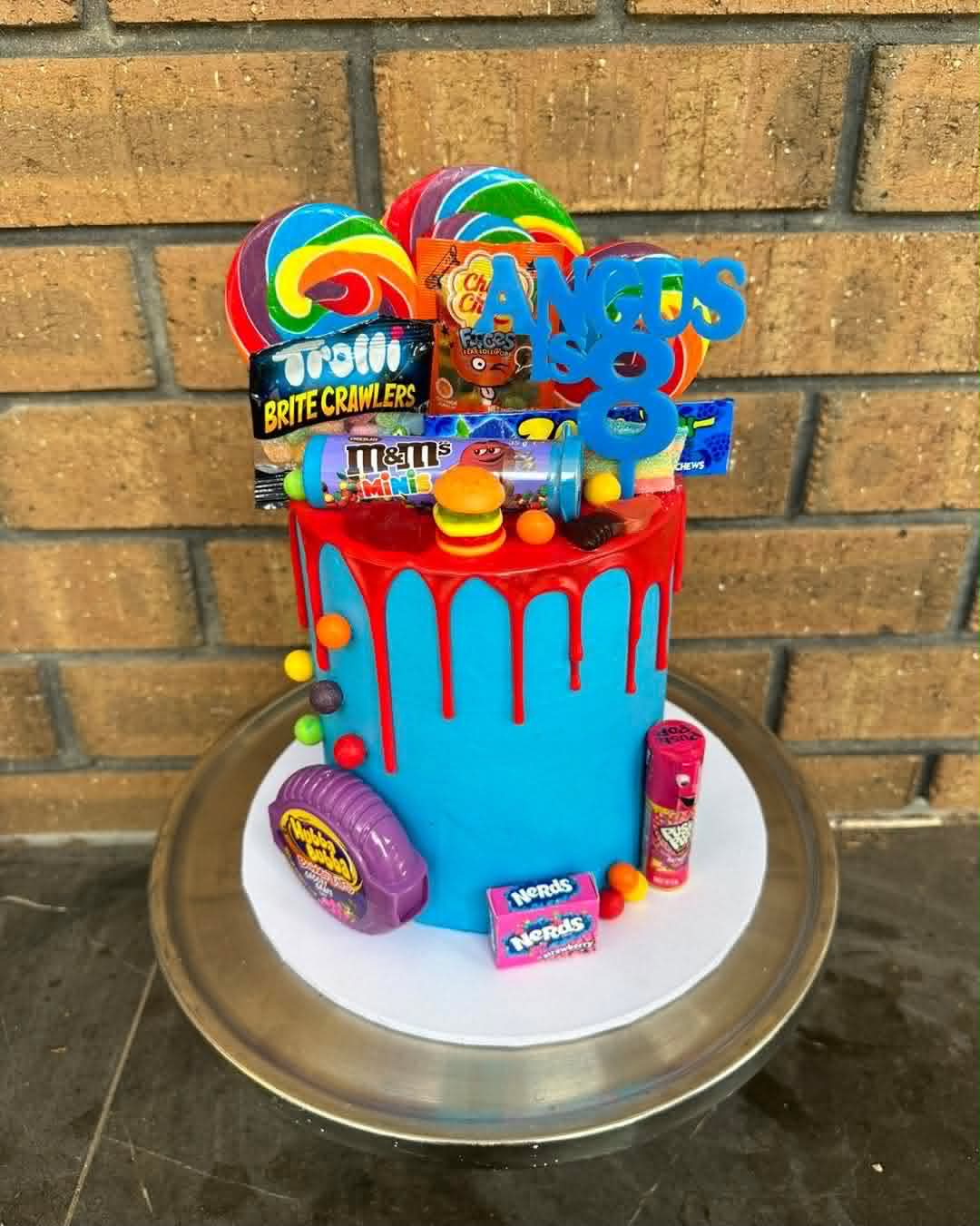 Blue lolly explosion birthday cake for Angus Is 8 with rainbow lollipops, M&Ms, Trolli worms, Nerds and candy bar toppers