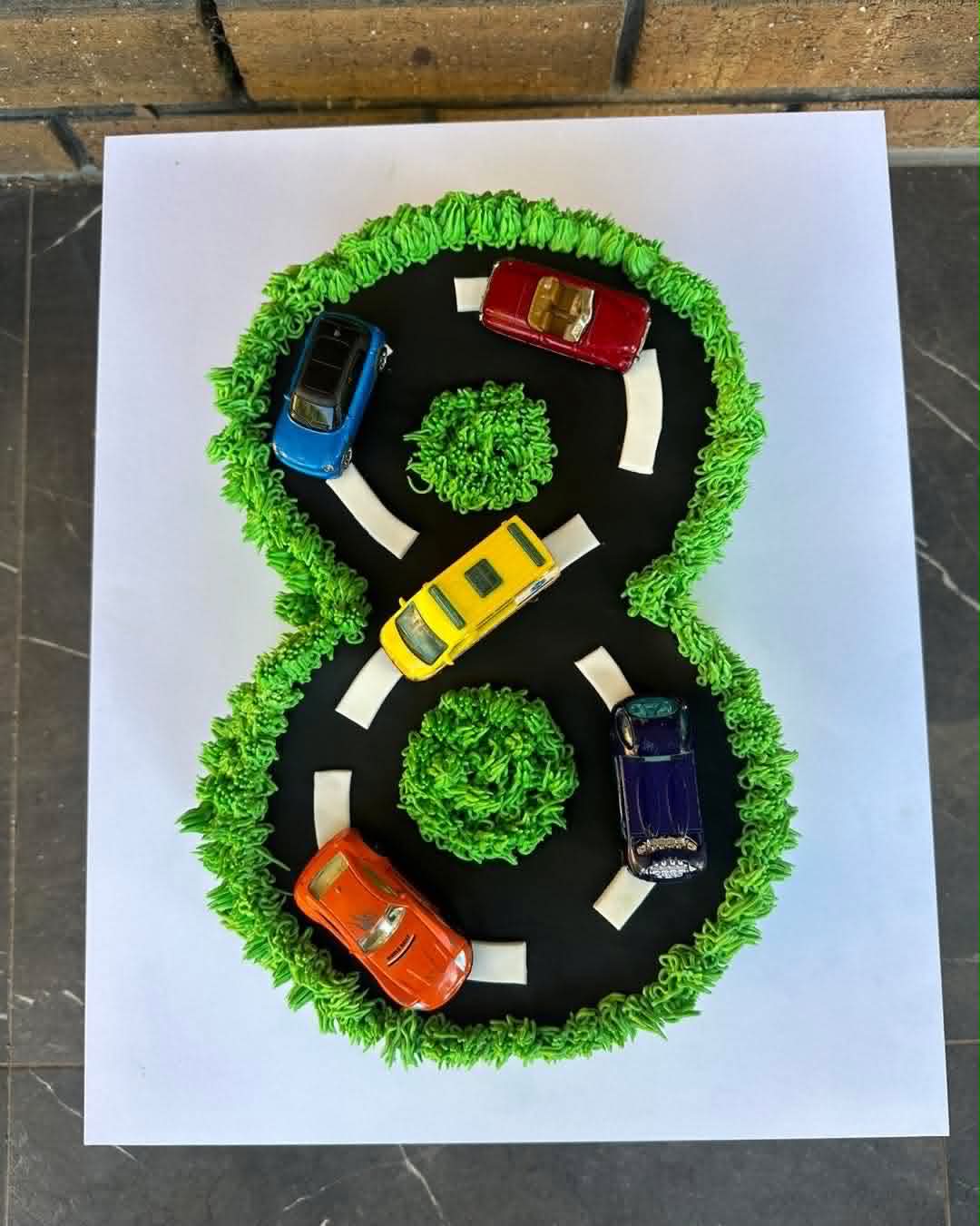Number 8 shaped race track birthday cake with green grass buttercream border and Hot Wheels car toppers