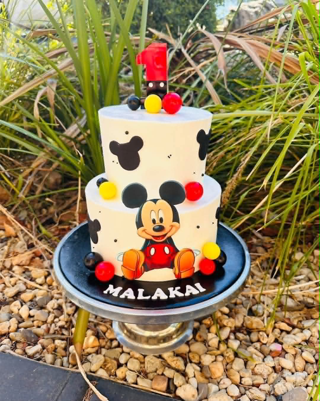 Two-tier white Mickey Mouse birthday cake for Malakai's 1st with Mickey silhouette fondant, red number 1 topper and coloured ball clusters