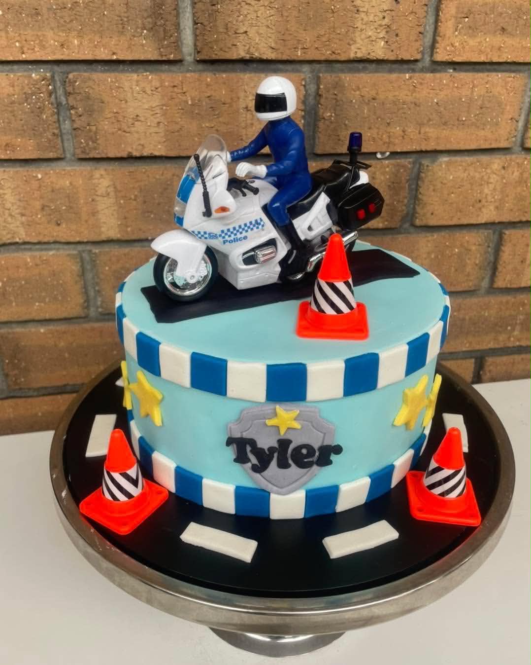Police motorbike birthday cake for Tyler with blue and white checkered fondant, traffic cones and police badge