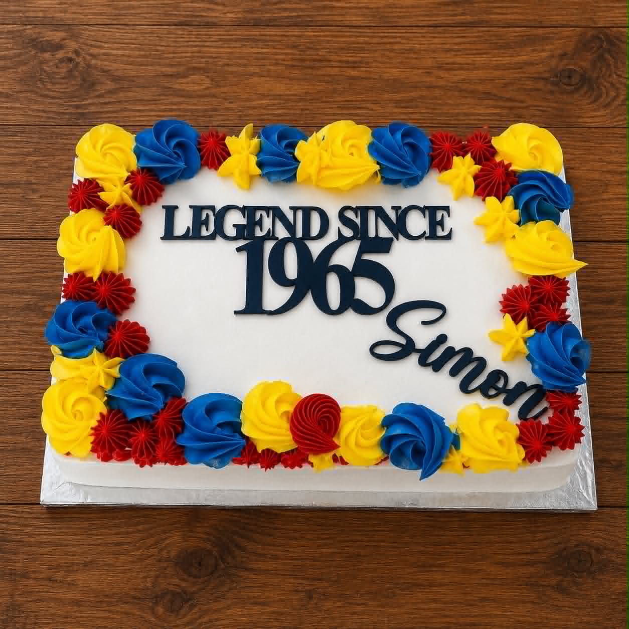 White slab cake with red, yellow and blue buttercream rosette border and Legend Since 1965 Simon acrylic topper