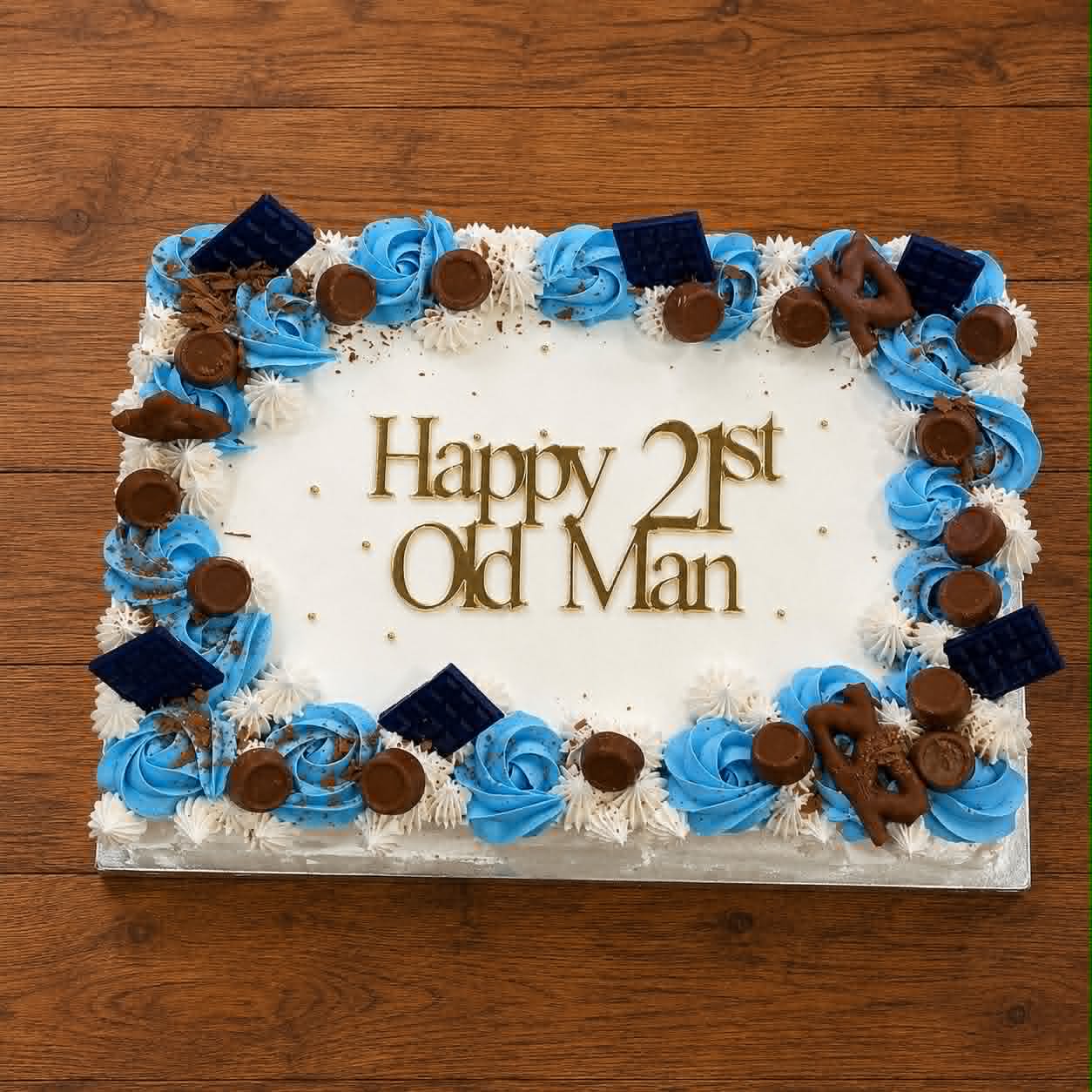 White slab cake with blue and white buttercream rosette border, Rolo and dark chocolate bar toppers and Happy 21st Old Man gold acrylic topper