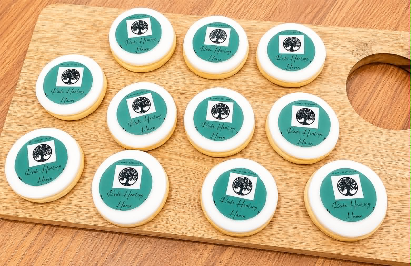 Round white sugar cookies with teal Reiki Healing Haven tree logo edible print arranged on a wooden chopping board