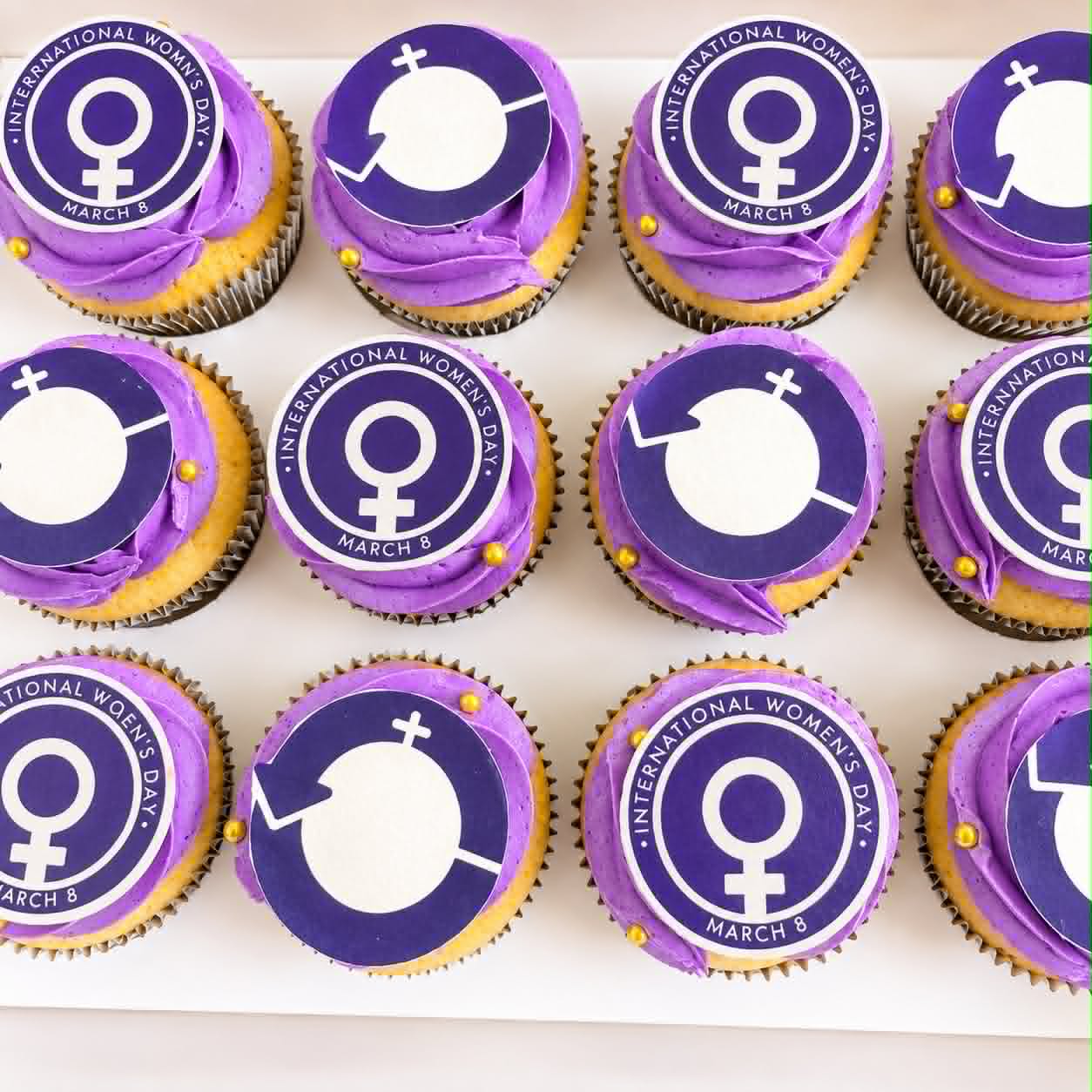 Purple buttercream cupcakes with International Women's Day March 8 edible print toppers and gold pearl balls