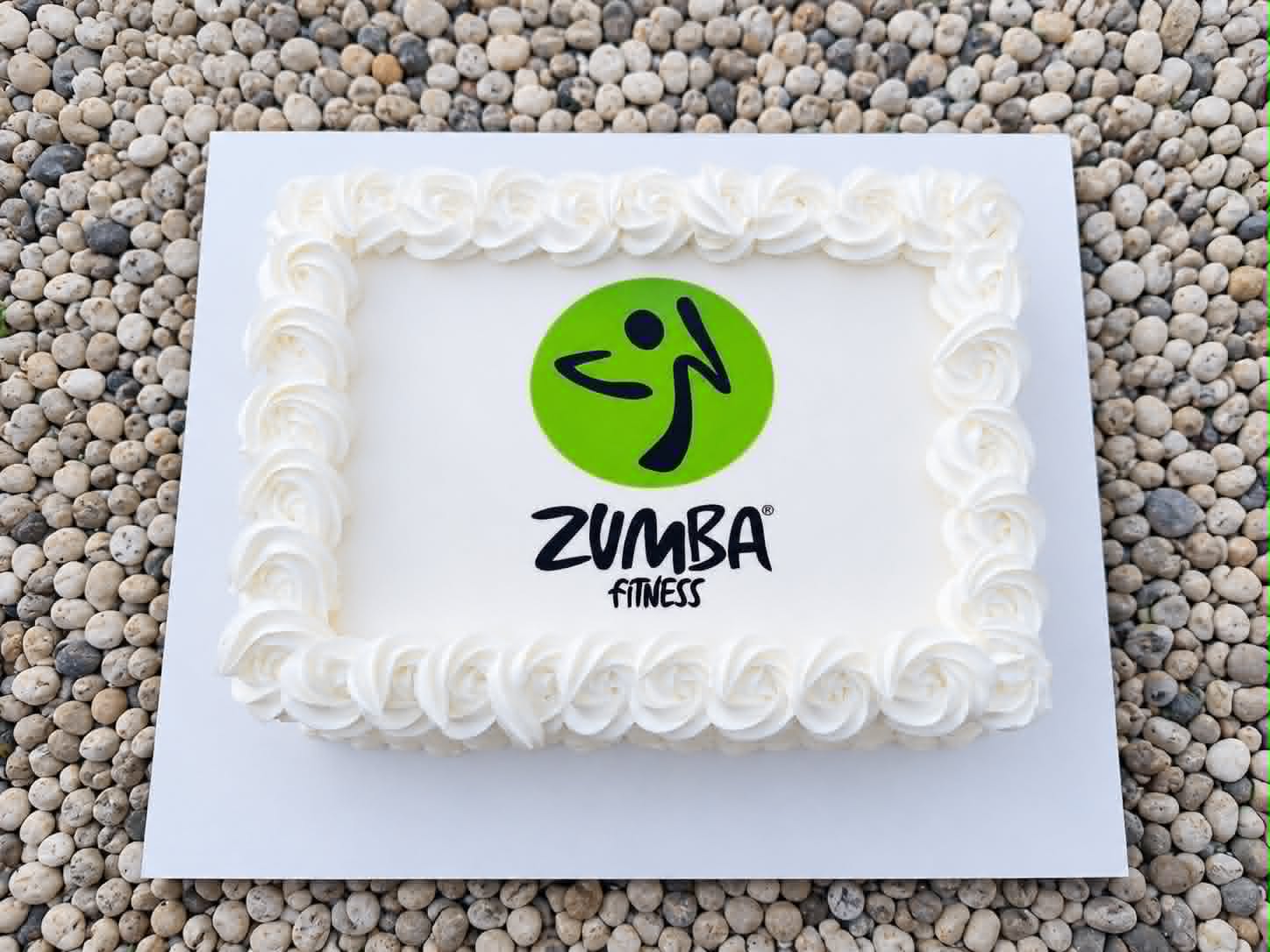 White rectangular slab cake with rosette border and Zumba Fitness green circle logo edible print in the centre on a pebble background